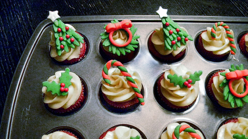A photo of cupcakes decorated with holiday wreathss and trees.